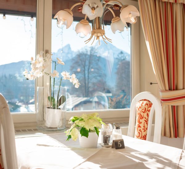 Gedeckter, sonniger Esstisch mit weißer Orchidee und Topfpflanze, Nummernschild 5, Blumenlampe und Bergblick.