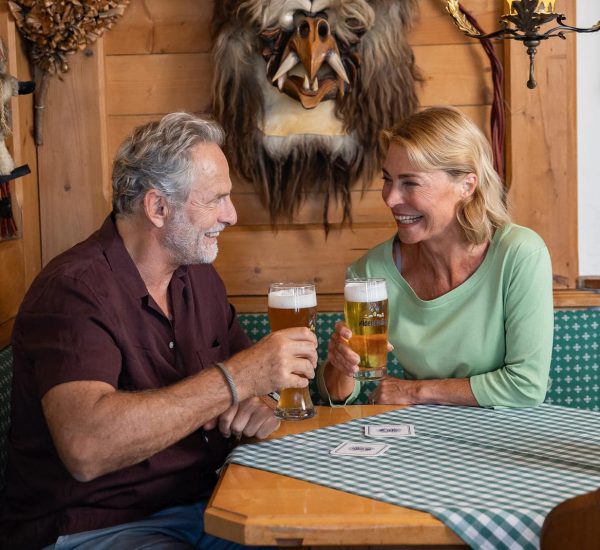 Älteres Paar lacht und stößt mit zwei Biergläsern an in einer gemütlichen Holzstube