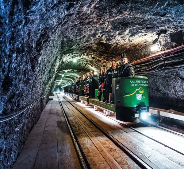 Grüne Besucherbahn des Salzbergwerks Berchtesgaden mit Fahrgästen in einem beleuchteten Stollen auf Schienen.