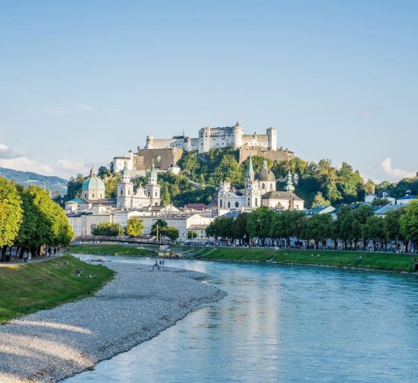 Blick auf Salzach und Salzburger Altstadt mit barocken Kirchenkuppeln und der Hohensalzburg-Festung auf einem Hügel.