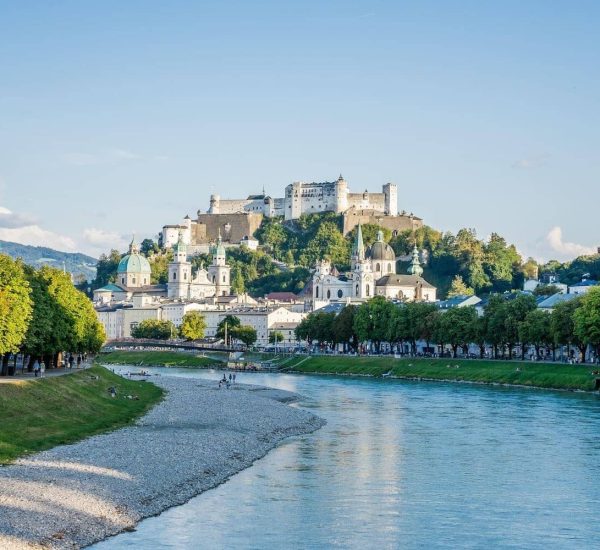 Blick auf Salzach und Salzburger Altstadt mit barocken Kirchenkuppeln und der Hohensalzburg-Festung auf einem Hügel.