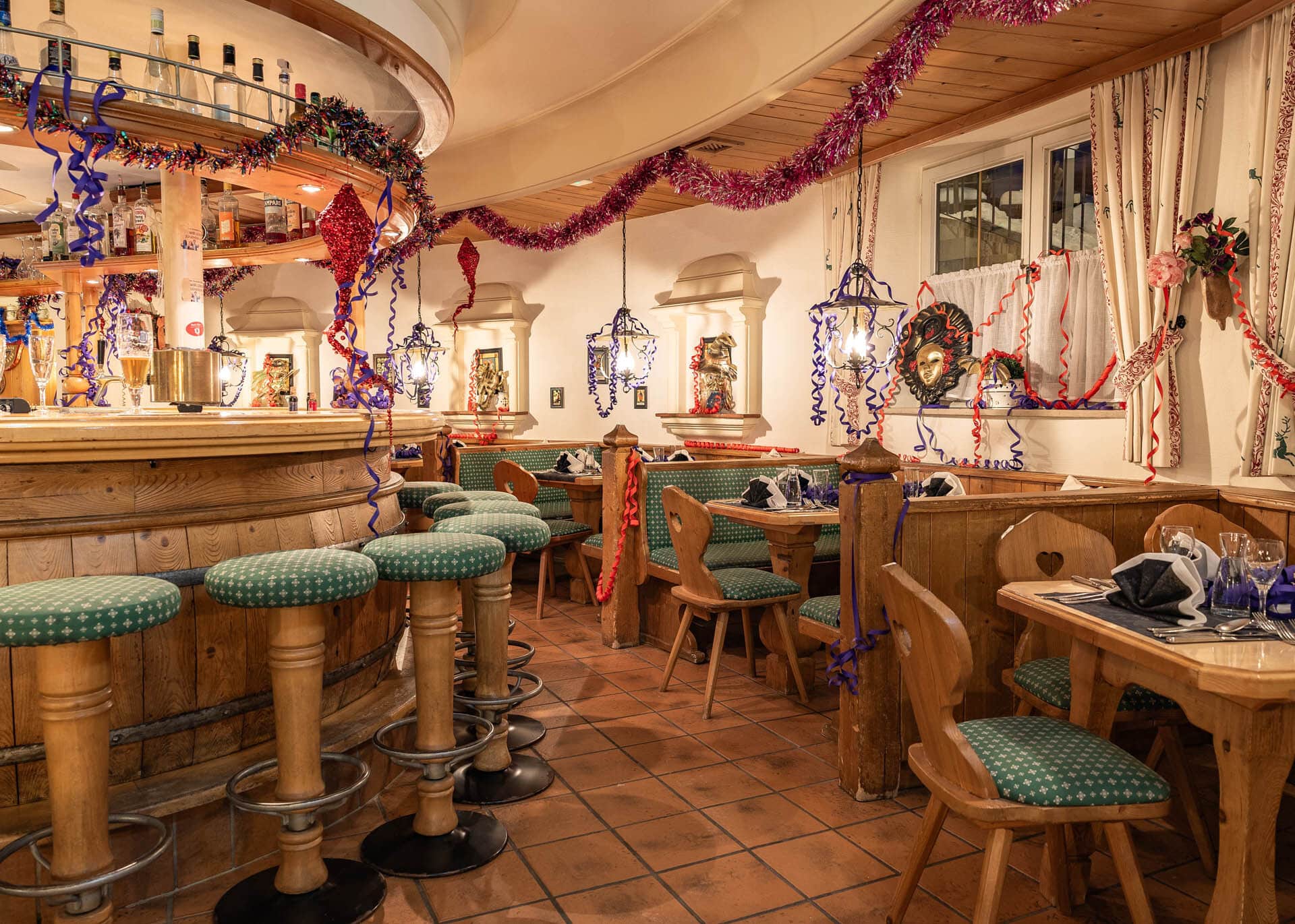 Gemütliche, rustikale Bar/Restaurant mit Holztheke, grünen Polsterhockern, Festdekorationen aus Lametta und Luftschlangen.